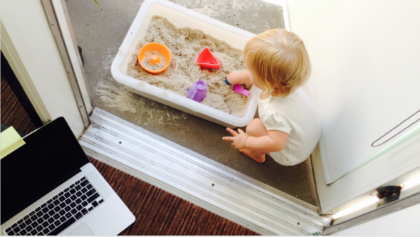 baby playing in sandbox next to an open laptop on the floor